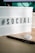 A lightbox sign displaying the word '#SOCIAL' in bold black letters on a desk surface. Next to it, there is a black pen and a round button with a cartoonish face. The background includes a part of a computer monitor and its cords.
