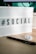 A lightbox sign displaying the word '#SOCIAL' in bold black letters on a desk surface. Next to it, there is a black pen and a round button with a cartoonish face. The background includes a part of a computer monitor and its cords.