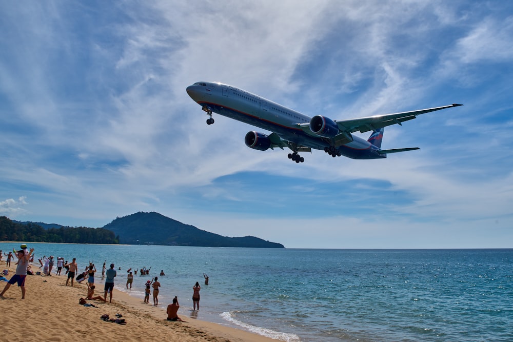 a large jetliner flying over a beach next to the ocean