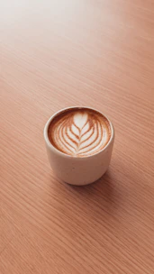 Close-up of a steaming latte with intricate leaf art on top, set against a dark wooden table.