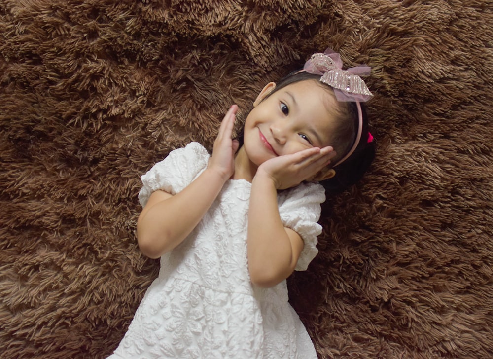 a little girl laying on top of a brown rug