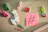 A variety of colorful stationery items and small toys are arranged on a light wooden surface, including a white llama with a colorful design, vibrant clothespins, paperclips, a red geometric shape, and a cactus. A pink sticky note with a black hashtag symbol is also present.