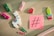 A variety of colorful stationery items and small toys are arranged on a light wooden surface, including a white llama with a colorful design, vibrant clothespins, paperclips, a red geometric shape, and a cactus. A pink sticky note with a black hashtag symbol is also present.