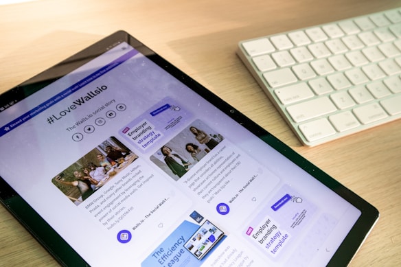 A tablet displaying a webpage with the hashtag #LoveWallsio prominently featured. The page includes images, text, and social media icons. Next to the tablet is a white keyboard placed on a wooden surface.