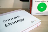 Two books are displayed on a wooden surface. The book in the foreground has a cover titled 'Content Strategy', while the book in the background is titled 'Graphic Design R: Revised Edition'.