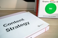 Two books are displayed on a wooden surface. The book in the foreground has a cover titled 'Content Strategy', while the book in the background is titled 'Graphic Design R: Revised Edition'.