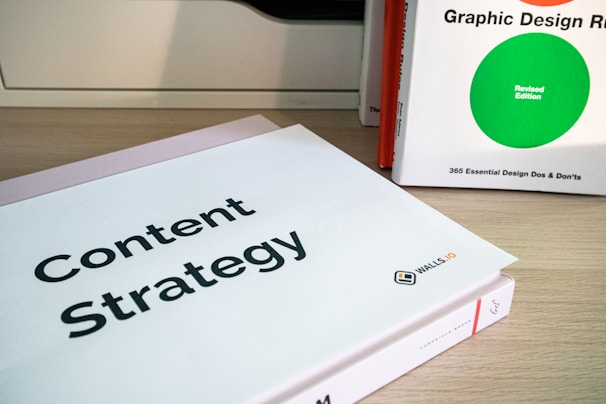 Two books are displayed on a wooden surface. The book in the foreground has a cover titled 'Content Strategy', while the book in the background is titled 'Graphic Design R: Revised Edition'.