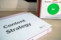 Two books are displayed on a wooden surface. The book in the foreground has a cover titled 'Content Strategy', while the book in the background is titled 'Graphic Design R: Revised Edition'.