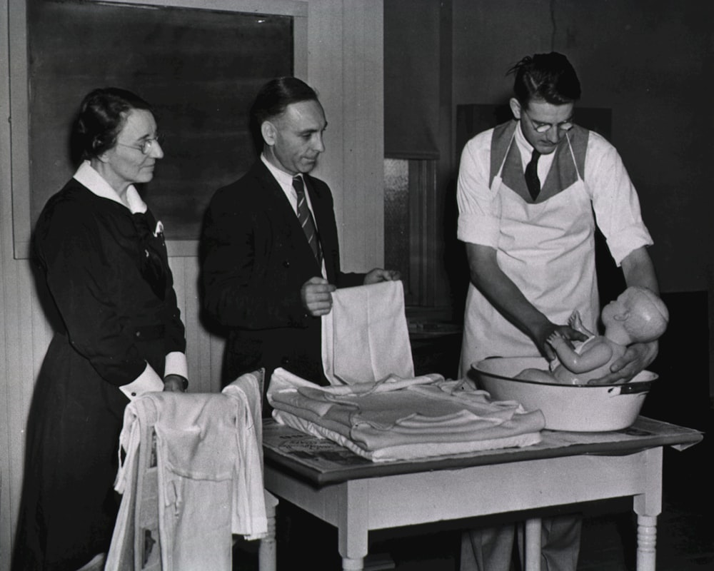 a black and white photo of three people in a kitchen