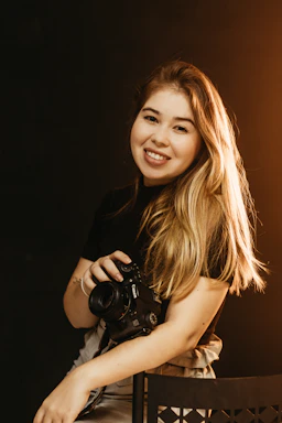 A friendly person holding a camera, smiling warmly at an event.