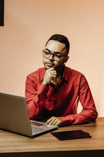A friendly student sitting at a desk, writing a message on a laptop with a warm, inviting background.