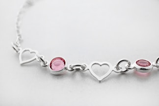 a silver bracelet with three hearts and a pink stone