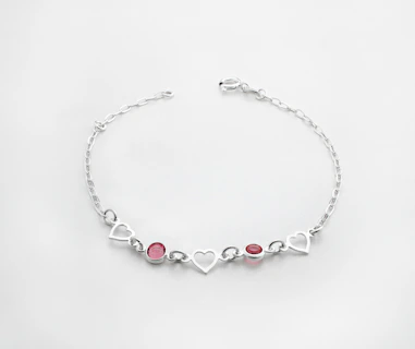 a silver bracelet with hearts and two red stones