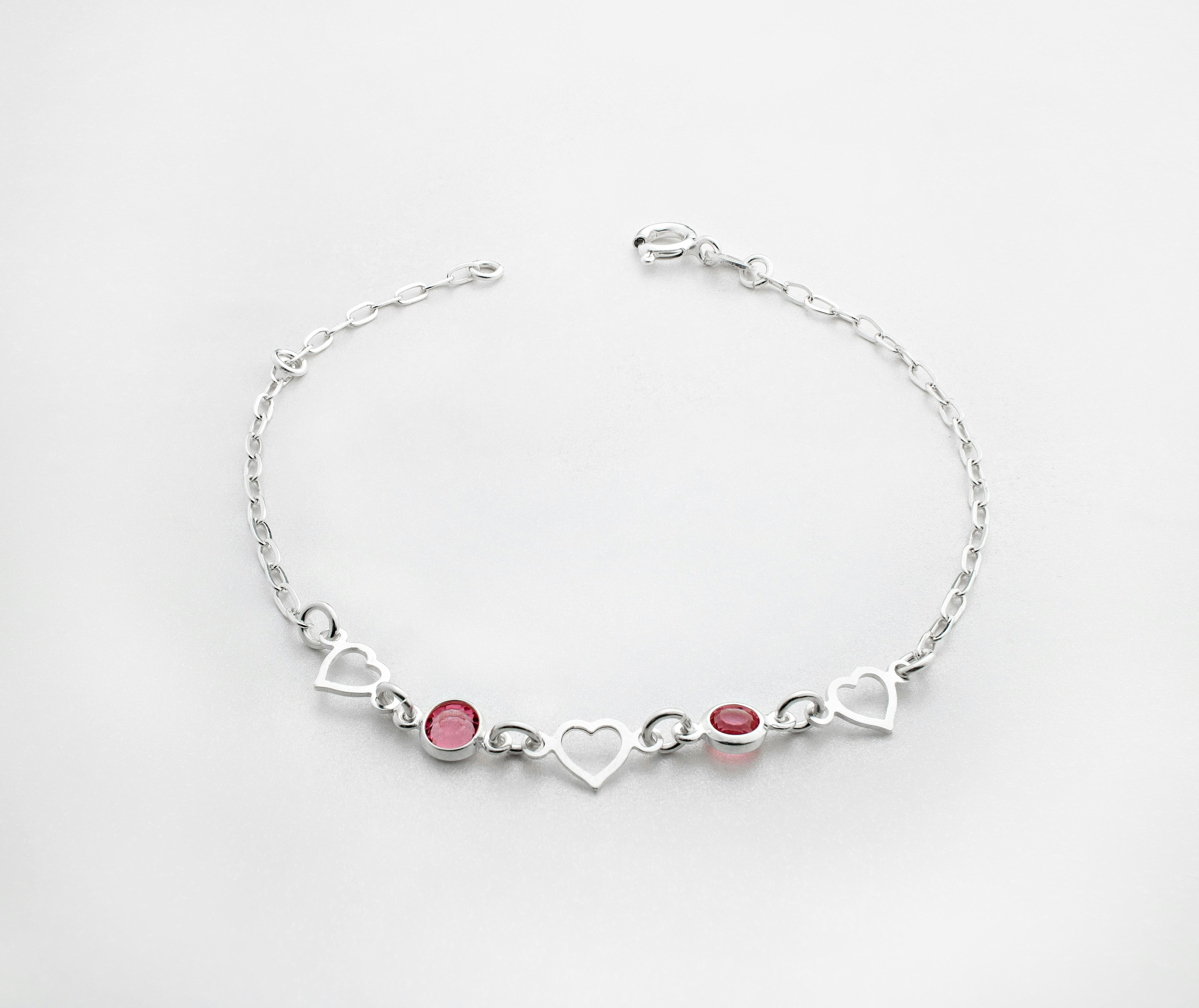 A silver bracelet in plain bright background with tiny red gems and silver heart-shaped pieces