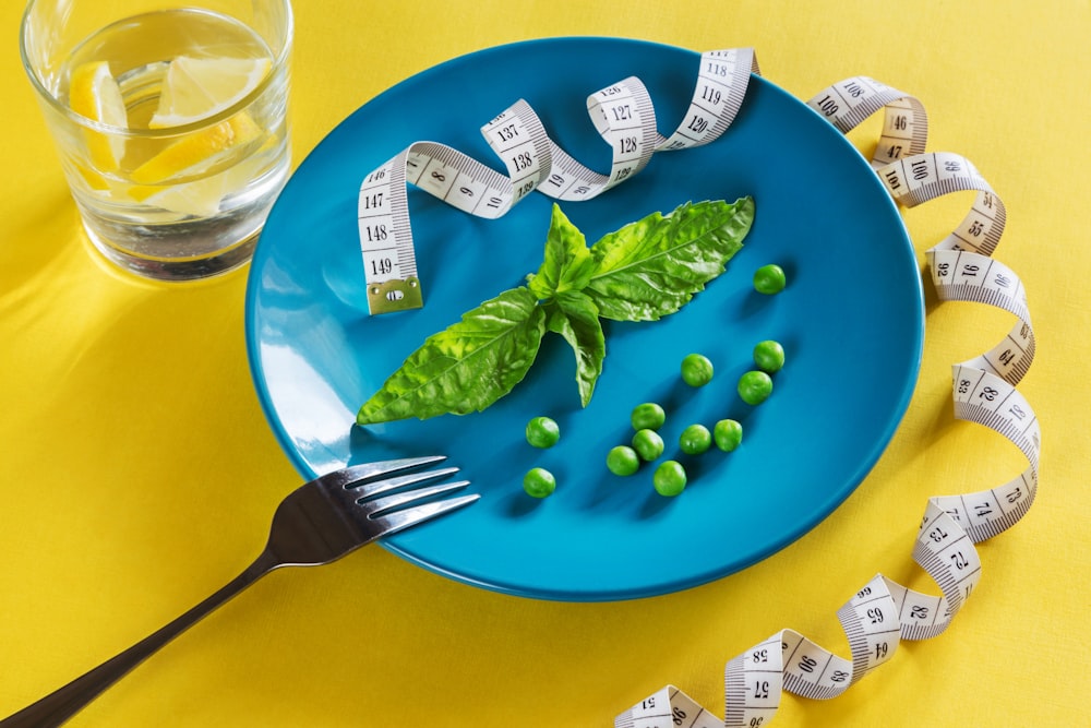 un plato azul cubierto con verduras verdes y cinta métrica