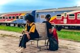 two people sitting on a bench in front of a train