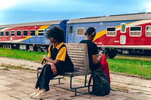 two people sitting on a bench in front of a train