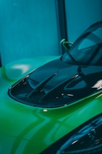 Close-up of a shiny black car hood with a fresh lime green paint touch-up.