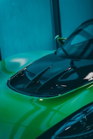 Close-up of a shiny black car hood with a fresh lime green paint touch-up.