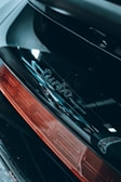 Close-up of a car's rear section featuring a shiny black surface with the word 'turbo' embossed above a red taillight.