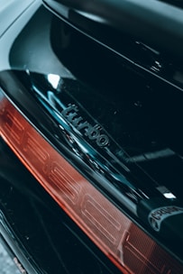 Close-up of a car's rear section featuring a shiny black surface with the word 'turbo' embossed above a red taillight.