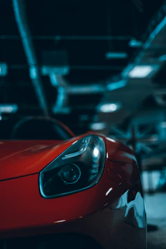 Close-up of a sleek supercar's headlight glowing under garage lights.