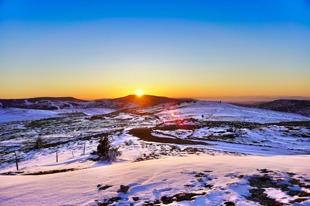 the sun is setting over a snowy mountain