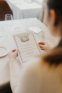 Hands holding a delicately designed menu with restrained typography in a cozy dining setting.