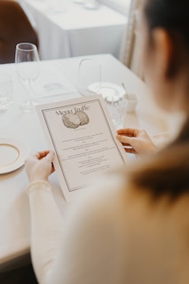A person is holding a menu titled 'Menu Truffe' at a dining table set with glassware, a plate, and a butter dish. The setting appears elegant and refined, suggesting a fine dining experience.