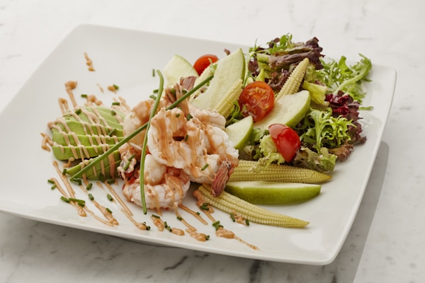 A white plate topped with a salad covered in shrimp