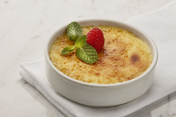 A rustic plate featuring a creamy brûlée topped with caramelized peppers and fresh basil leaves.
