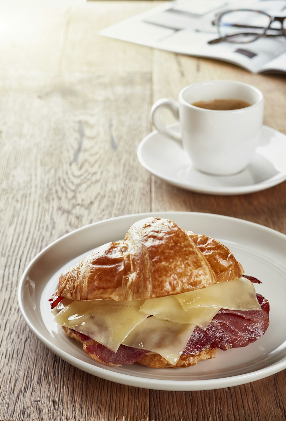 a white plate topped with a sandwich next to a cup of coffee