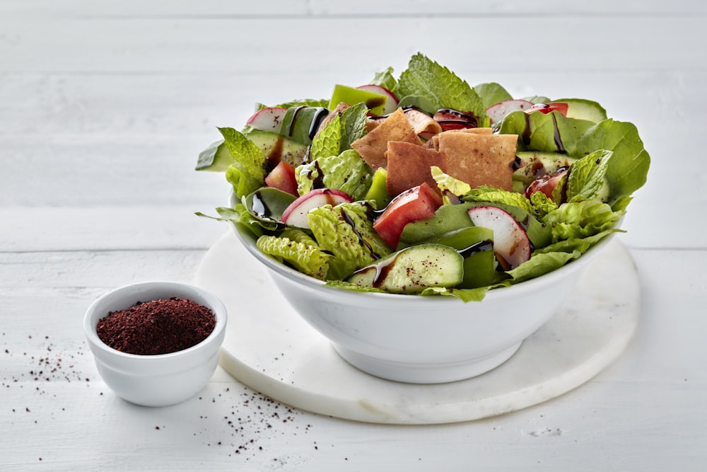 a white bowl filled with a salad next to a small bowl of dressing