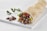 A neatly arranged wrap placed on a white rectangular board. The wrap is filled with colorful ingredients including lettuce, tomatoes, yellow bell peppers, and some meat, with a garnish of parsley on the side. A small piece of meat and a sprig of parsley rest beside the wrap on the board.