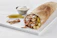 Close-up of a loaded shawarma wrap with fresh veggies and sauce dripping temptingly