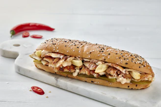 a sandwich with meat, cheese, and peppers on a cutting board