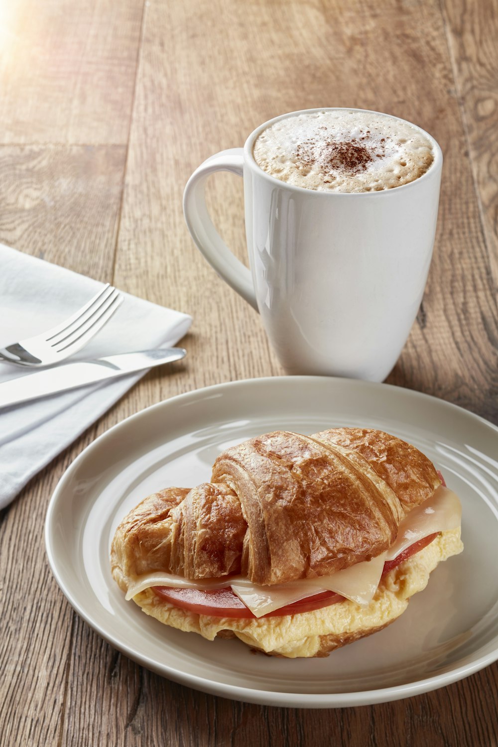 un panino con croissant su un piatto accanto a una tazza di caffè
