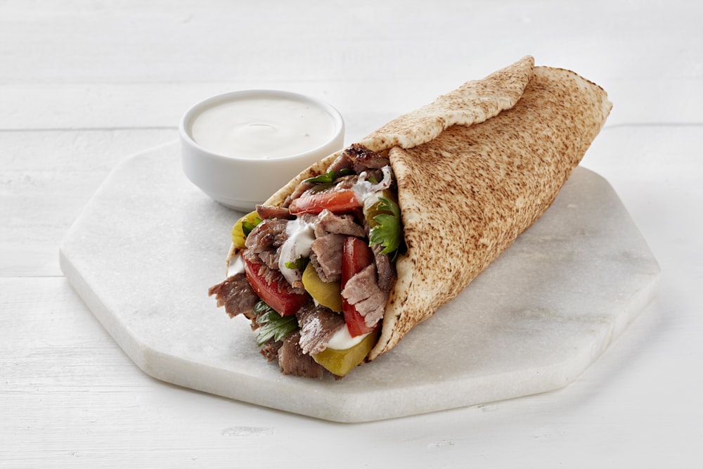 Un sandwich pita sur une assiette avec un petit bol de vinaigrette ranch