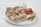 Several rolled flatbreads filled with sliced chicken are placed on a white round serving tray. Accompanying them are sliced tomatoes, pickles, and a small bowl of creamy sauce.