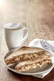 A steaming cup of rich coffee beside a perfectly toasted sandwich on a rustic table.