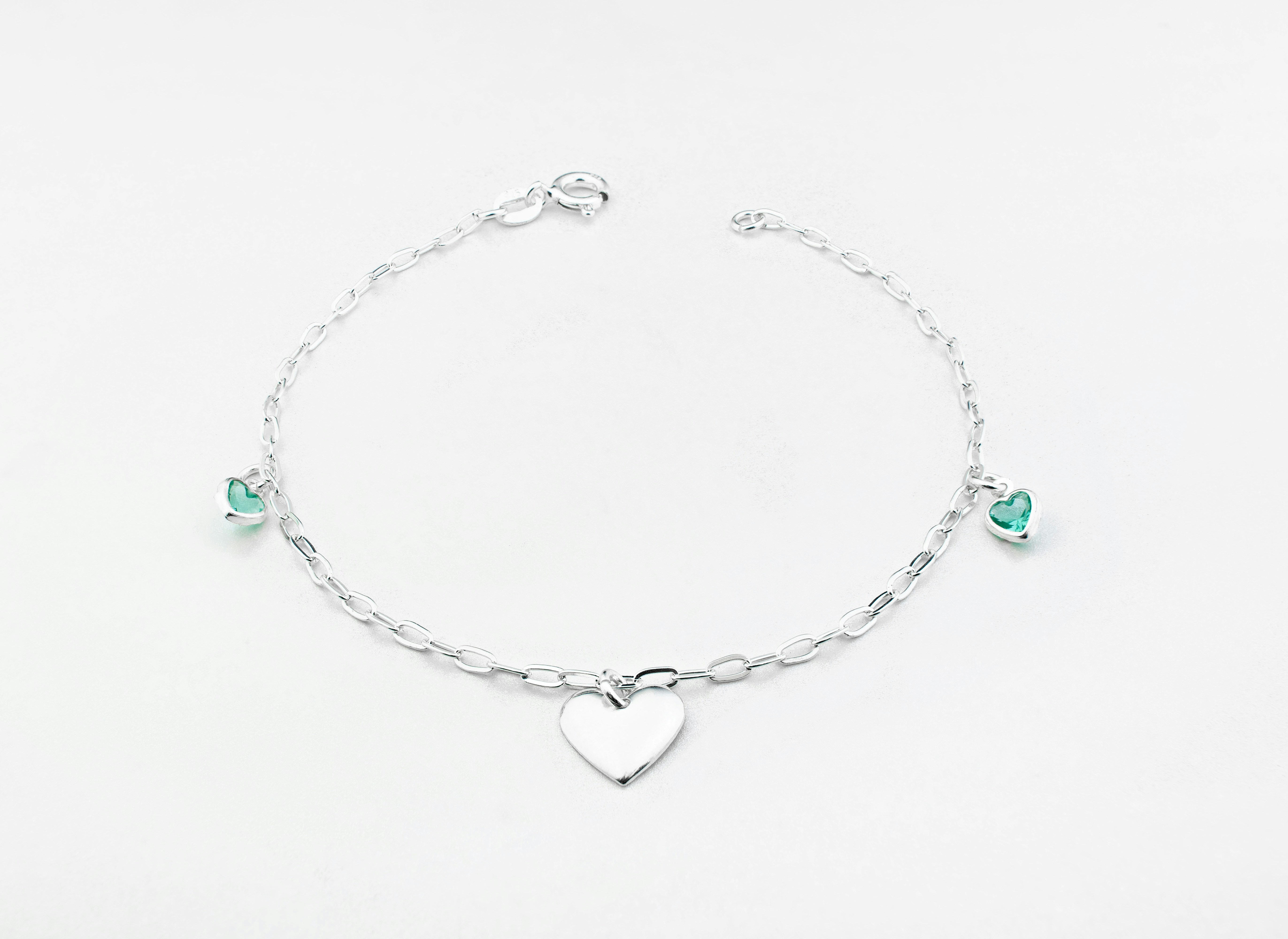 Silver bracelet on plain bright background with tiny green heart-shaped gems
