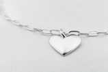 Elegant silver necklace with a minimalist pendant shining under soft, warm lighting on a charcoal black surface.