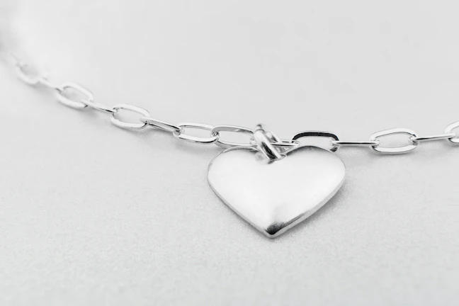 Close-up of a minimalist silver pendant with a smooth matte finish against a soft white background.
