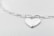 A heart-shaped silver pendant attached to a glossy chain with oval links, set against a soft, light gray background. The whole setup gives a minimalist and elegant impression.