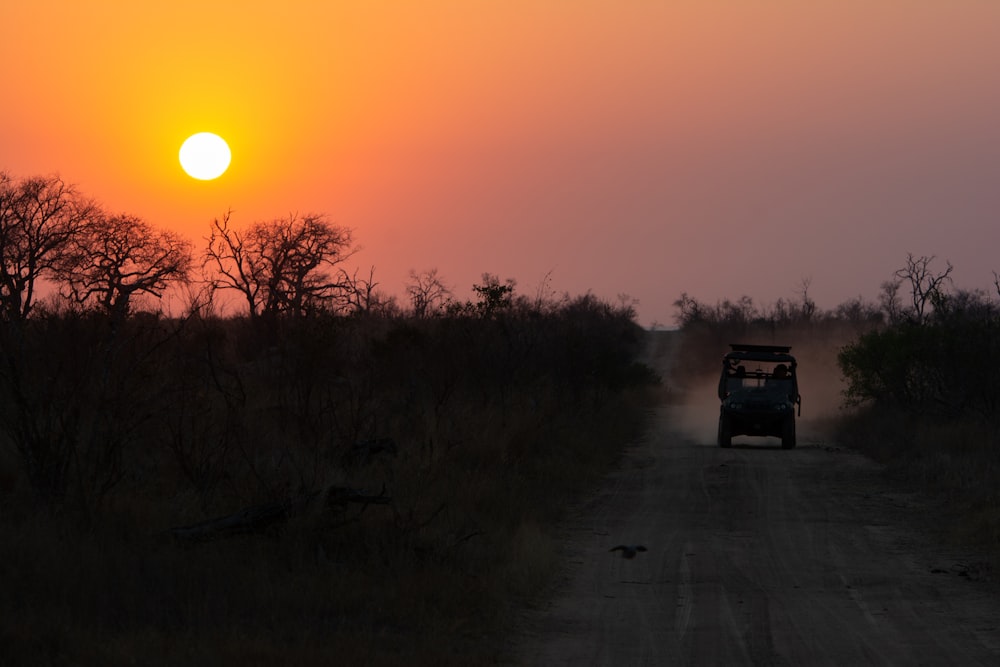 a jeep driving down a dirt road at sunset