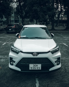 A clean, modern Toyota Yaris parked with palm trees and turquoise water in the background.