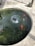 A round pond containing several brightly colored fish, likely koi. The water ripples from a small central fountain, creating circular patterns. The pond is surrounded by a concrete edge, and there's a small stone frog statue observing near the edge.