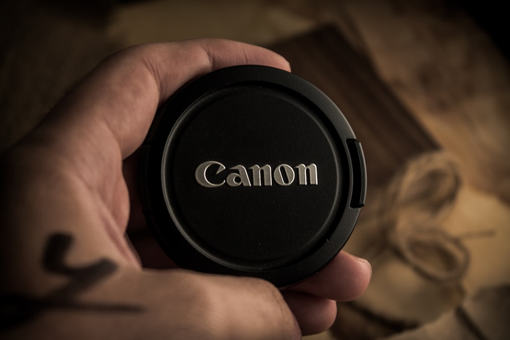 a person holding a camera lens cap in their hand