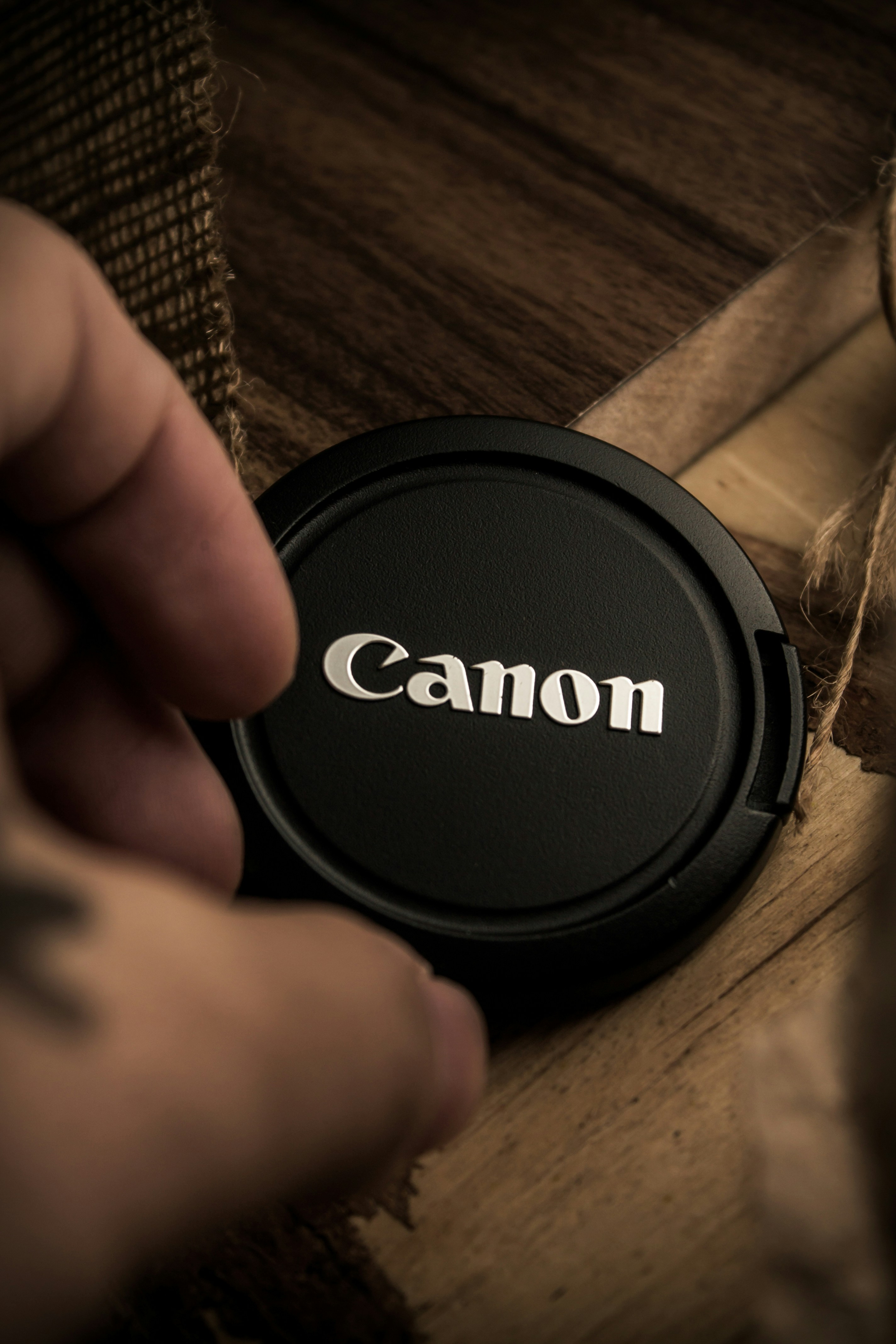 a person holding a camera lens cap with the word canon on it