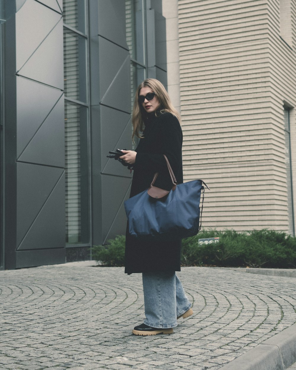 a woman walking down a street holding a blue bag